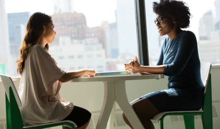 two women sitting beside table and talking