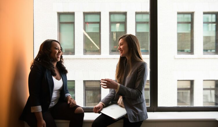 two woman sitting by the window laughing